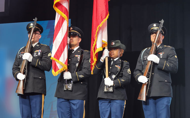 Cuatro militares están de pie presentando la bandera estadounidense y la bandera de Texas.